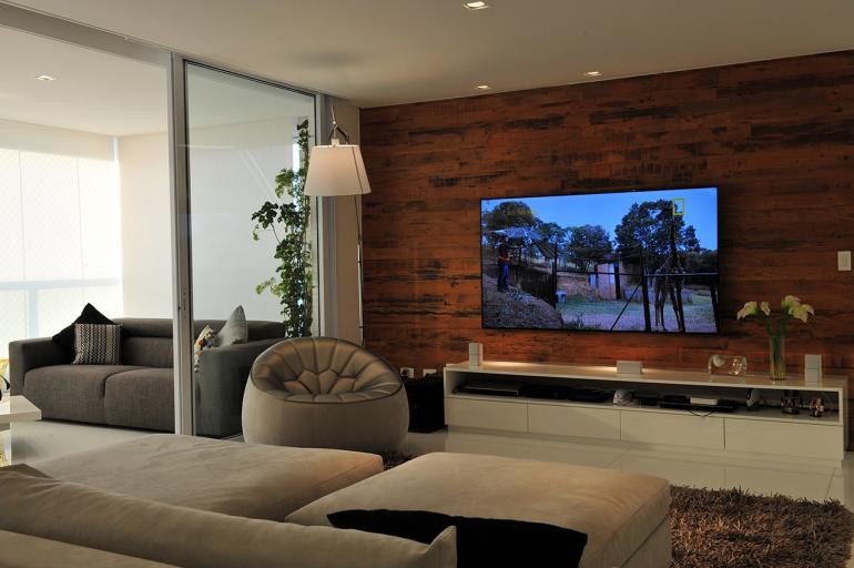 Celina Germer - A sala de estar recebeu um amplo painel de madeira em toda extensão da parede.